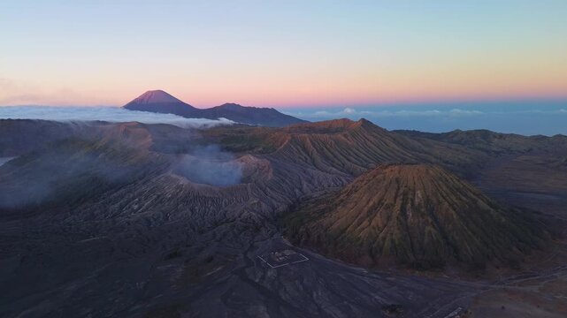 Drone orbit around Mount Bromo during morning twilight, revealing the volcanic landscape, Mount Semeru and layered blue-to-pink sky above the Tengger caldera, Indonesia