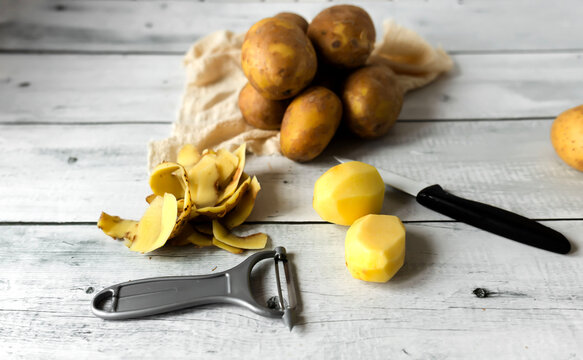 Peeling raw potatoes with a knife and vegetable peeler on a white wooden table