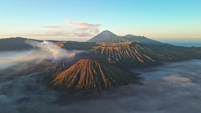 Drone orbit around Mount Bromo in vivid morning light, revealing a sea of clouds, Mount Semeru and abundant volcanic smoke across the Tengger caldera, Indonesia