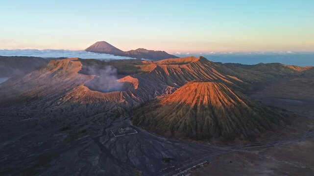 Drone slowly approaches the Mount Bromo volcanic landscape in vibrant red dawn light, revealing Mount Bromo, Mount Semeru, surrounding peaks and the Tengger caldera, Indonesia
