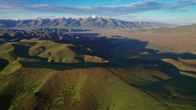 Aerial panorama of green rolling hills and snowcapped mountains under blue sky