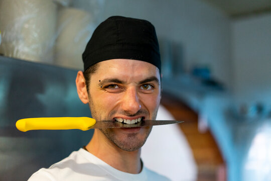 Portrait of cook in kitchen with knife between his teeth