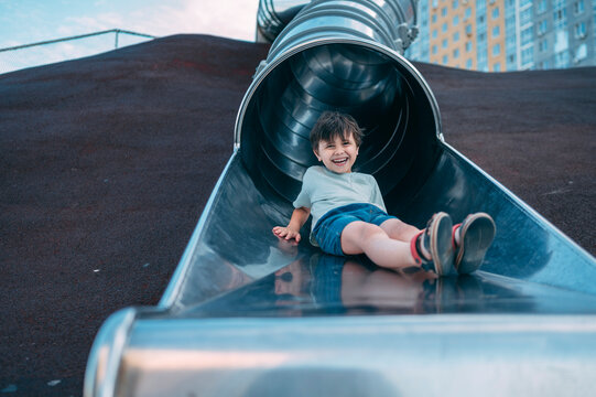 Happy boy rides a metal slide at the outdoor playground