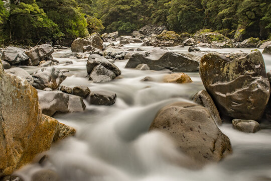 Clear flowing mountain river water cascading rapidly over smooth grey wet rocks in a scenic valley