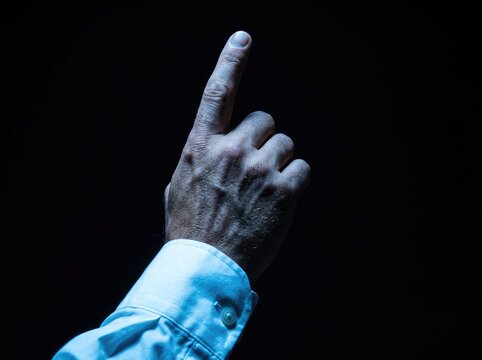 Dust covered hand in white shirt pointing upward against black background