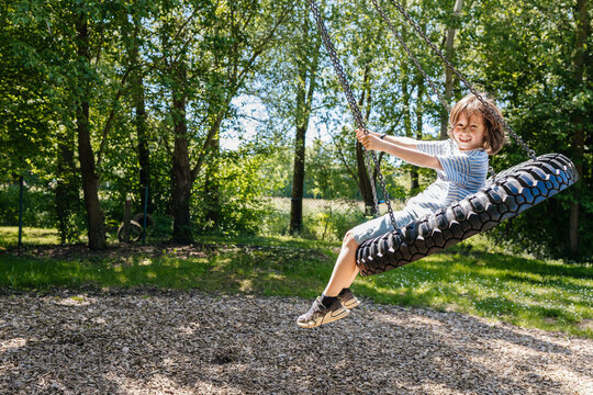 Happy child playing on a tire swing at the playground in summer