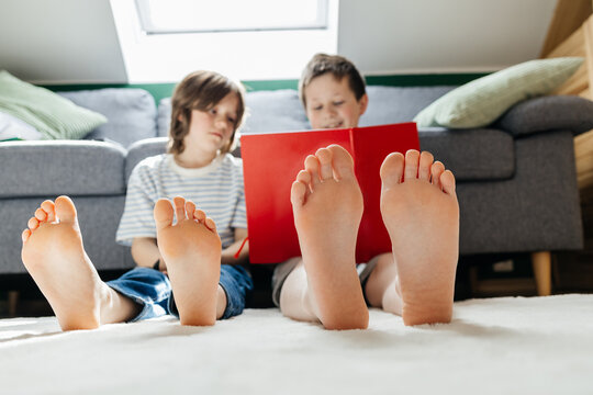 Two boys read a book on the floor with bare feet in the foreground