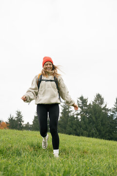 A happy woman runs through a grassy meadow during a fall hiking trip