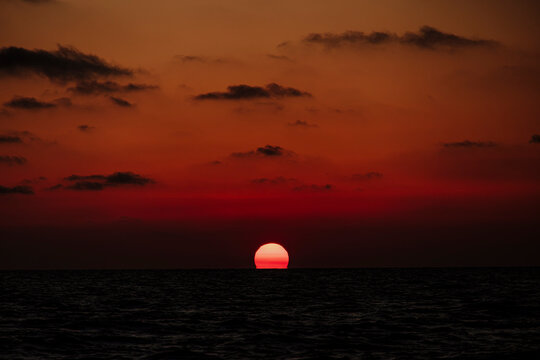 The red sun sets over the dark ocean horizon