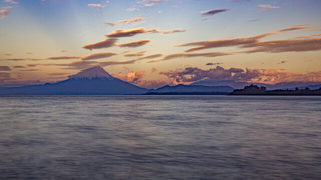 Volcanic mountain silhouette over calm water at sunset golden hour with mountain landscape twilight