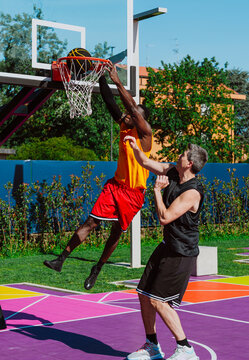 A man dunks a basketball over a defender on a colorful outdoor court