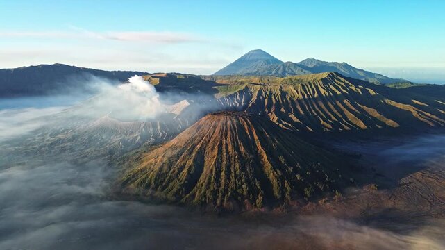 High drone orbit over Mount Bromo, revealing the expansive volcanic landscape, smoking Bromo crater, Mount Semeru and a sea of clouds across the Tengger caldera, Indonesia