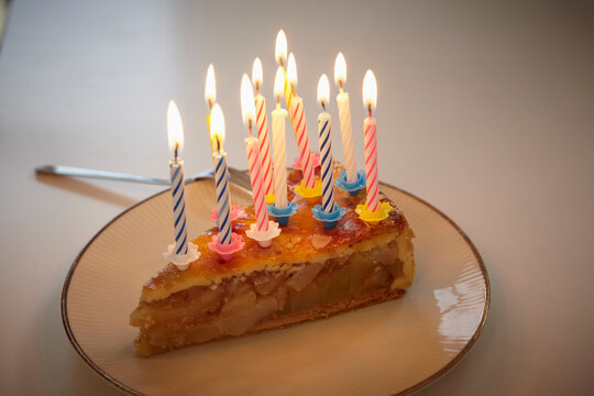 A slice of birthday cake with lit candles sits on a plate in Cologne
