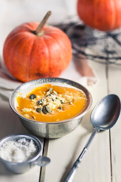 Bowl of Exotic pumpkin soup with coconut milk and coconut flakes on white wood