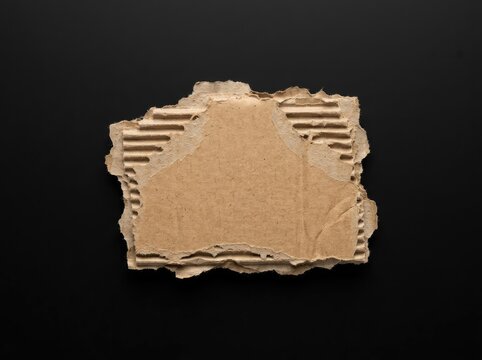 Torn corrugated cardboard piece on a dark background ideal for graphic layouts symbolizing raw texture sustainability and creative minimalism
