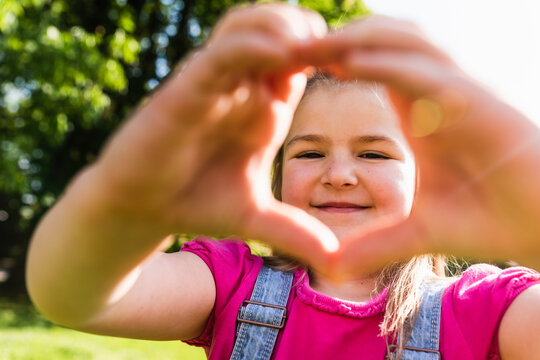 Portrait of smiling girl shaping a heart with her hands in park
