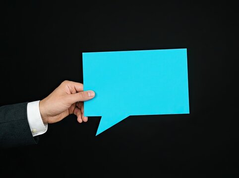 Hand holding a blue speech bubble on black background ideal for business marketing content representing communication dialogue and feedback
