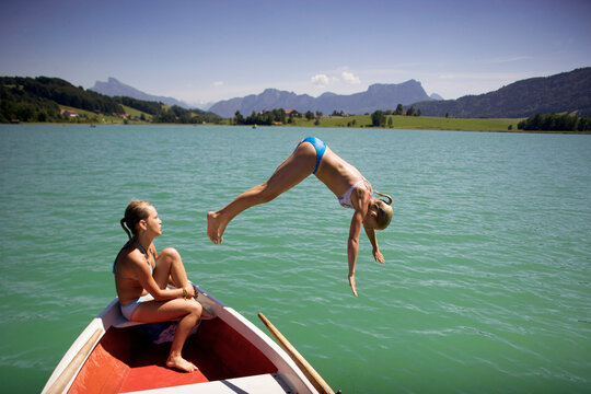 Young girl in rowing boat with friend, jumping into lake