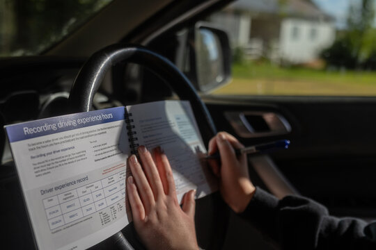 Person sitting in car writing practice hours in driver experience record logbook