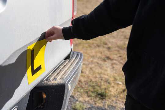 Person attaching yellow learner driver L plate to back of vehicle