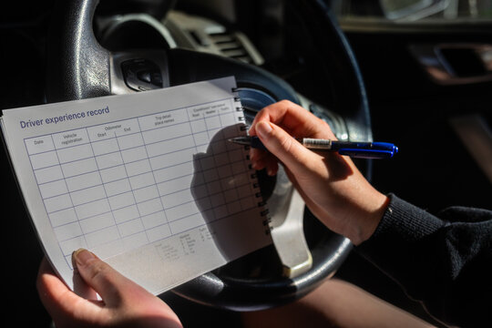 Person sitting in car writing trip and condition details on driver record logbook