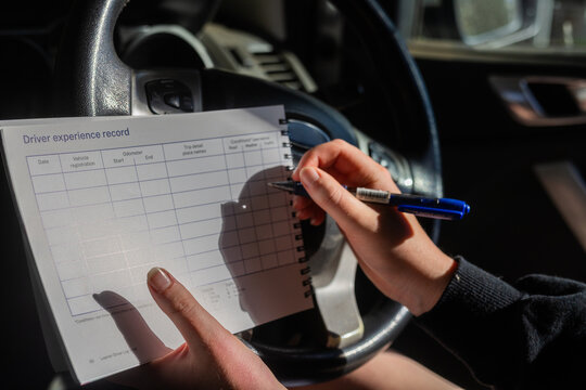 Person sitting in car preparing to write on driver experience record logbook