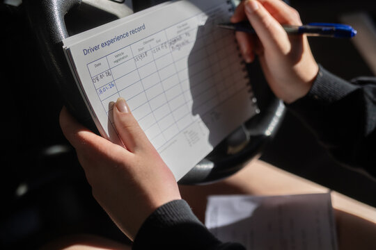Person sitting in car writing mileage data on driver experience record form