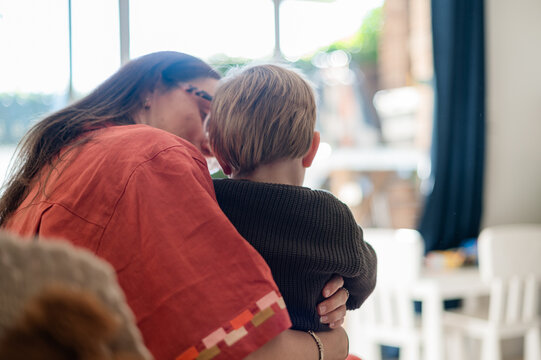 Mother holding toddler son on her lap while seated on the couch in a cosy living room