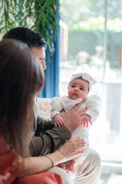 Father holding newborn baby girl while seated with mum on the sofa