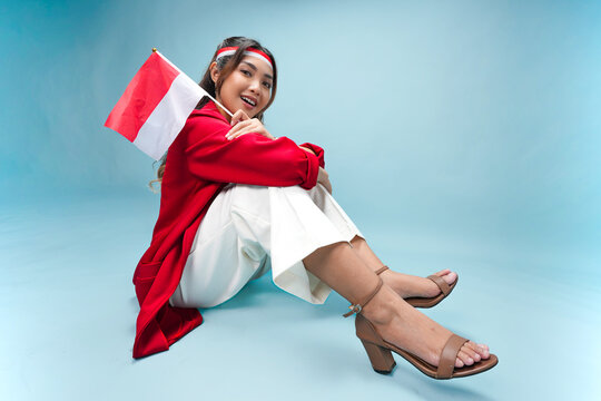 Attractive Indonesian woman is sitting and holding mini country flag while smiling to the camera.