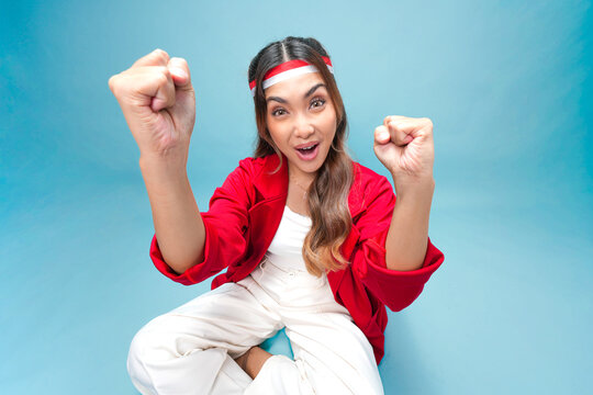 Excited Asian woman is raising fists doing celebration while sitting on the floor.