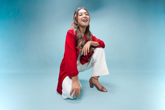 Pretty Indonesian woman is sitting on the floor and posing smiling to the camera.