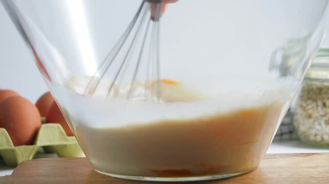 Close-up of milk and eggs being whisked together in a glass bowl, preparing a smooth mixture for homemade cooking and baking.