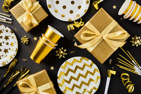 Golden birthday party decor and gifts on black background flatlay