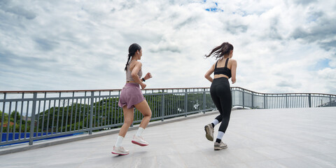 Naklejka premium Two Asian women running together on outdoor bridge for fitness workout