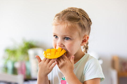 Little Australian girl eating a freshly cut mango fruit in kitchen at home