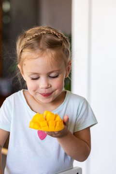 Little Australian girl eating a freshly cut mango fruit in kitchen at home