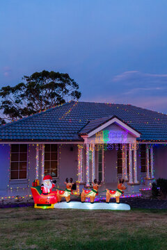 Merry Christmas sign on house with coloured fairy lights and blow up Santa sleigh decoration