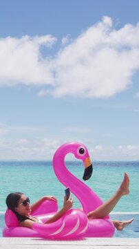 Vacation woman on inflatable Flamingo float mattress using phone in swimming pool. Girl relaxing on travel holidays at resort pool in bikini. Raw unedited video of real woman model without makeup