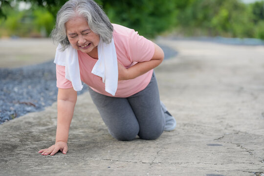 Senior woman chest pain medical emergency outdoor pavement kneeling towel, older adult clutching chest during exercise, fatigue and distress in park