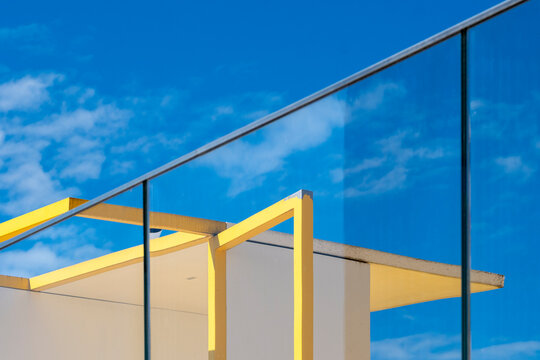 Yellow canopy structure against blue glass and open sky creates a bold geometric contrast in a minimal modern architectural composition