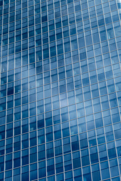 Blue glass facade with repeating windows and subtle reflections forming a clean geometric grid across a modern high rise building exterior