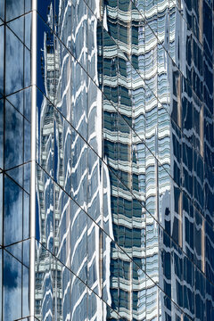 Reflective glass facade with distorted tower reflections and vertical lines forming an abstract pattern across a modern office building exterior