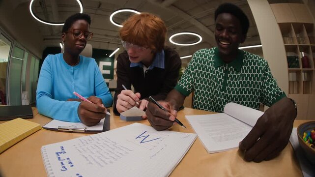 Multiethnic young adults collaborating on project, writing in notebook and discussing ideas, POV bottom view. Footage is perfect for educational marketing or diversity in workplace campaigns