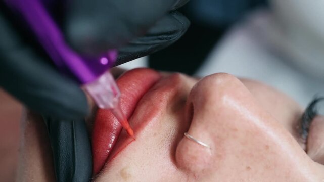 Extreme close up of a permanent makeup artist performing a lip blush tattoo procedure with a PMU machine in a professional beauty salon.