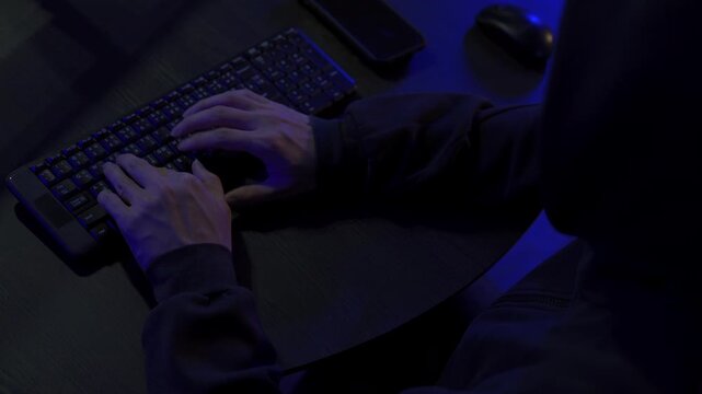 Close up of hacker's hand typing code on computer in a dark room.