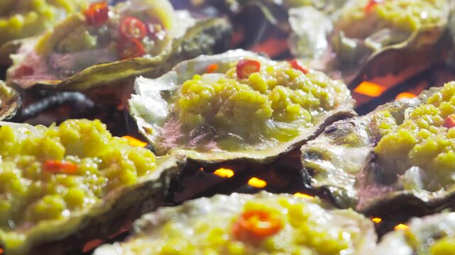 Grilled oysters with garlic sauce and chili on charcoal barbecue