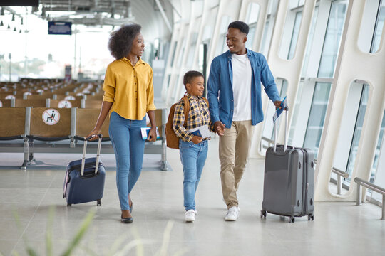 A smiling African American family with a young son walks together through a modern airport terminal, ready for their vacation or journey