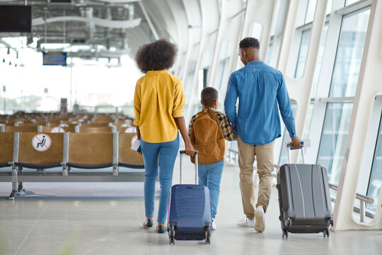 A diverse family with a child walks through a modern airport terminal, pulling suitcases and carrying backpacks, anticipating their journey