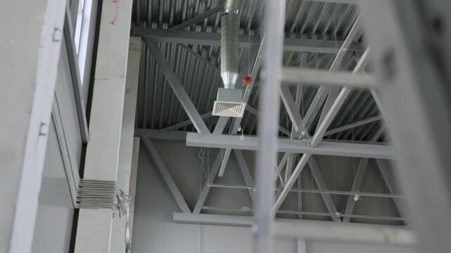 Galvanized air ventilation pipes extends down from metal roof trusses. Perforated cable trays and steel beams form busy framework